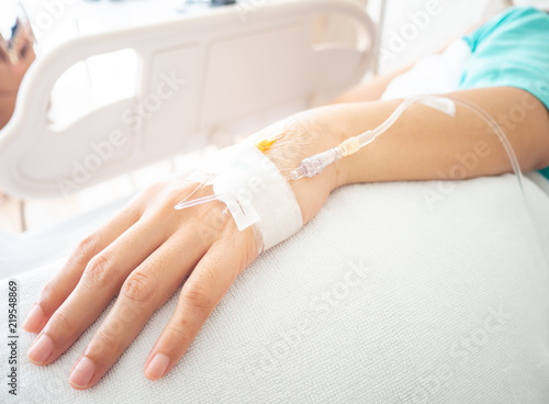 Close up hand of asia woman patient with intravenous catheter for injection plug in hand during lying in the hospital bed.