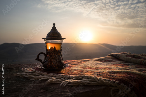 Arabska herbata w szkle na wschodnim dywanie. Koncepcja wschodniej herbaty. Puchar tradycyjny Armudu. Zachód słońca w tle. Selektywne ustawianie ostrości