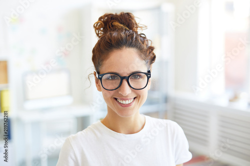 Happy young businesswoman in eyeglasses and white t-shirt gives you toothy smile