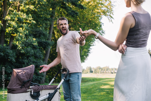 cropped image of mother smoking cigarette near baby carriage in park, father yelling at her