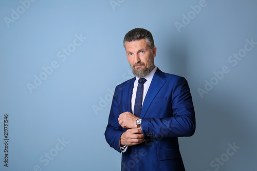 Handsome mature man in elegant suit on color background