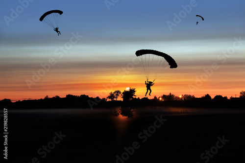 Spadochroniarze lądują na płycie lotniska aeroklubu po zachodzie słońca.