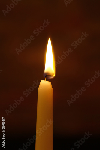 cute wax burning candle with bright fire against the heavy black background.