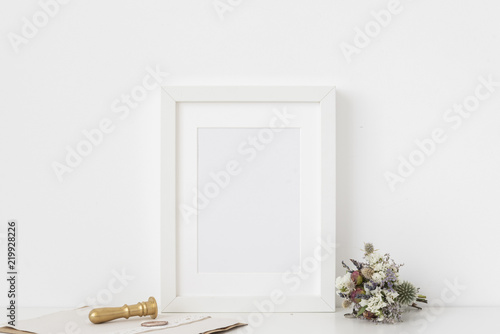Cute white a5 portrait frame mockup with bouquet of dried flowers, gold stamp and printing on white wall background. Empty frame, poster mock up for presentation design. 
