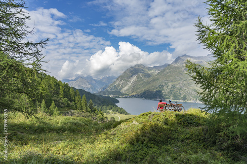 Senior woman, riding here e-mountain bike on the famous trails around the lakes in the upper Engadin, between Saint Moritz and Maloja, Engadin, Switzerland with stunning views on the lake of Silvaplan