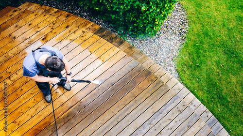 man cleaning terrace with a power washer - high water pressure cleaner on wooden terrace surface