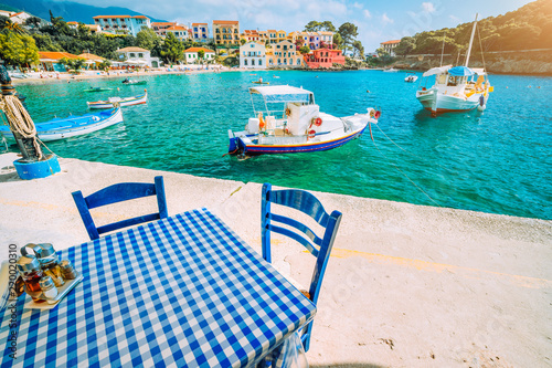 Traditional Greek restaurant with blue and white table and chairs at the sea coast of Assos village. Azure water, sunshine, summer feeling summer vacation