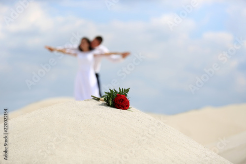 Bukiet z czerwonych róż i Młoda Para na szczycie piaszczystej wydmy.
