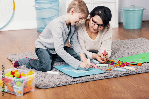 Mother and autistic boy drawing a picture on the floor at home