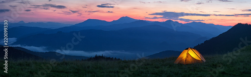 Glowing orange tent in the mountains under dramatic evening sky