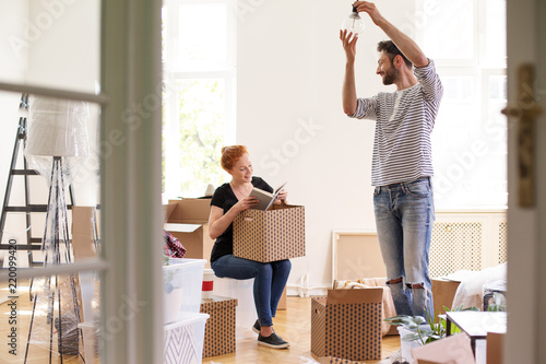 Man hanging lamp while smiling woman unpacking stuff from boxes