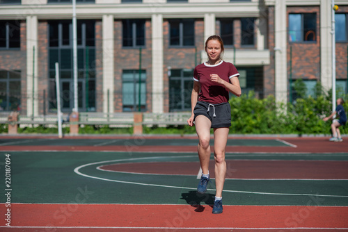 Red-haired young girl runs in the stadium. Student delivers standards for running outdoors. Young woman running on the football field