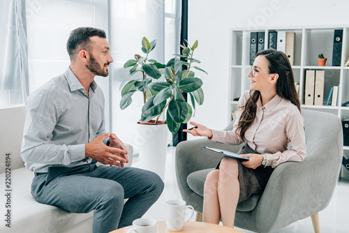 smiling psychiatrist with clipboard talking with happy patient in office