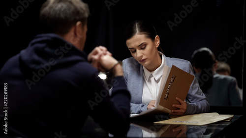 Young female police officer comparing suspect statements with file documents