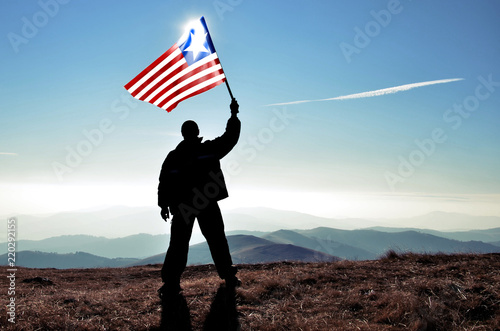 Successful silhouette man winner waving Liberia flag on top of the mountain peak