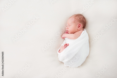 Cute newborn baby lies swaddled in a white blanket. Copy space and top view