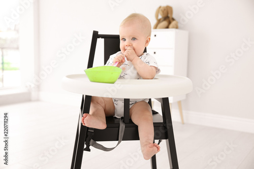 Cute little baby eating in high chair at home