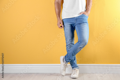 Young man in stylish jeans near color wall with space for text, focus on legs