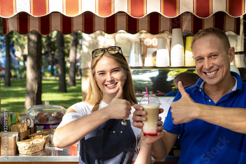 Man and woman barista with a glass of coffee in the park. Mobile coffee cart in the park