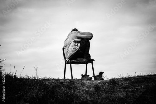 A poor refugee refugee in the Jungle field of Calais crouches hooded on a chair at the top of the hill taking off his shoes