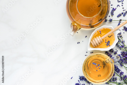 lavender tea in a cup and teapot with honey and fresh flowers over white marble table. herbal drink. top view