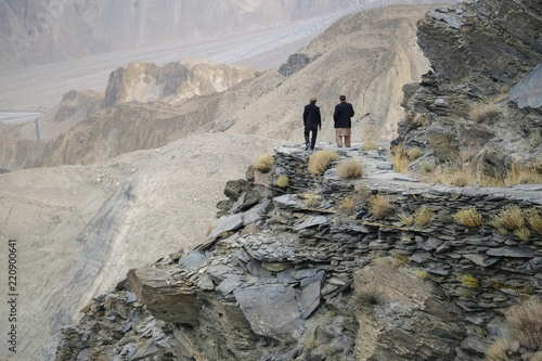 Two Pakistani men walking along Passu glacier trail amid Karakoram mounrain range, Hunza valley, Gilgit-Baltistan, Pakistan