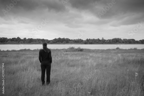 Eine anonyme Frau steht einsam auf einem Feld und blickt in die Ferne. Monochrom.