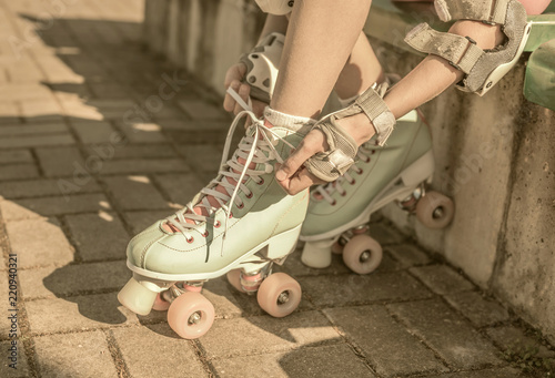Skater girl putting on mint retro roller skates outdoor