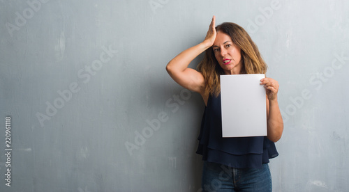 Middle age hispanic woman holding bank paper sheet stressed with hand on head, shocked with shame and surprise face, angry and frustrated. Fear and upset for mistake.