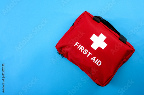 First aid treatment and medical emergency response concept with flat lay view of a red with a white cross first aid kit isolated on blue background with copy space for text