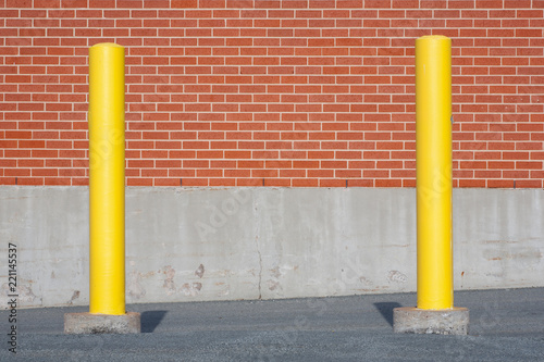 Yellow traffic bollards in front of brick building wall.