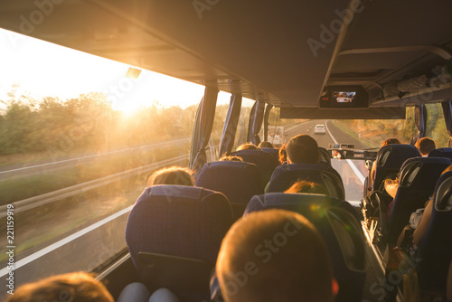 Background. Travel by bus. Bus interior. Salon of the bus with people fill the sun with light in the sunset. People travel on a big tourist bus. The bus rides along the mornings in the sunrise