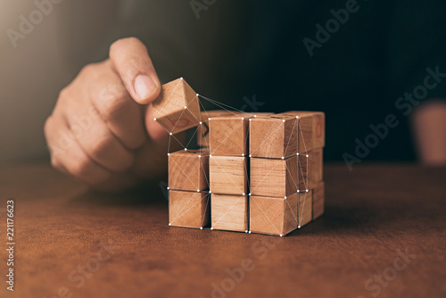 business man try to build wood block on wooden table and blur background business organization startup concept