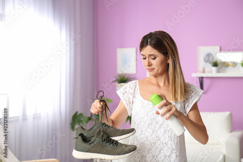 Woman spraying air freshener on shoes at home