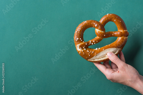 Young woman hold in hand German savory lye pretzel with salt on dark green background. Poster Banner for Bakery Coffee Shop Menu. Oktoberfest Card. Copy Space