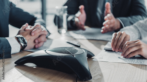 cropped shot of business people having conversation and using speakerphone at modern office