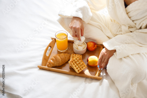 beautiful brunette in a dressing gown and a sweatshirt on her head is having breakfast in bed