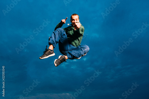 Sporty man trains parkour outdoor. Young parkour man jumping in park on a sunrise against a blue sky