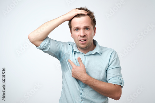 Young man in blue shirt with sweat trail on it. He is sweating becaise of hot temperature in office.