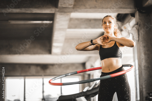 Beautiful caucasian young woman doing hula hoop in step waist hooping forward stance. Young woman doing hula hoop during an exercise class in a gym. Healthy sports lifestyle, Fitness, Healthy concept.