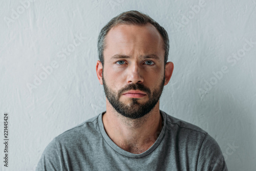 portrait of unhappy bearded man looking at camera on grey