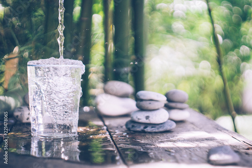 Clean water pouring into the glass next to the stones on the old wooden table. Japanese style. Cleansing and detox concept