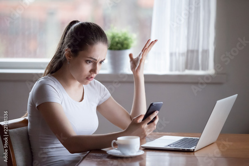 Mad young female annoyed with scam or spam messages on smartphone, frustrated woman receive bad news on cell, confused girl get phone problems having no signal, bothered with not working device