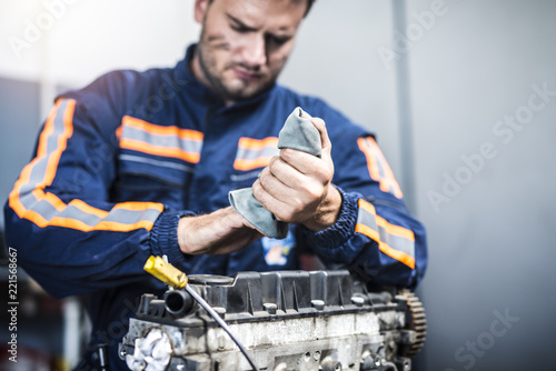 Serious professional mechanic wiping hands with rag after hardworking on car engine. Service and maintenance. 