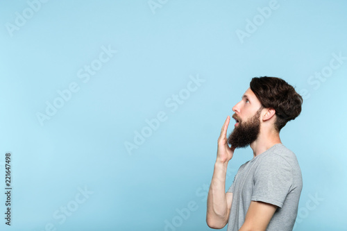 man looking sideways and is shocked or impressed by smth on the left. free space for advertisement or text. portrait of a bearded guy on blue background.