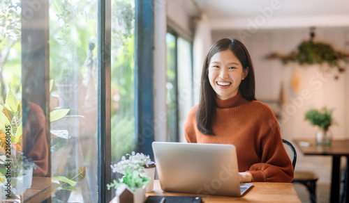 Happy young Asian girl working at a coffee shop with a laptop