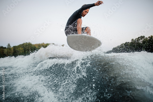 Active wakeboarder jumping on the blue splashing wave against the background of clear sky