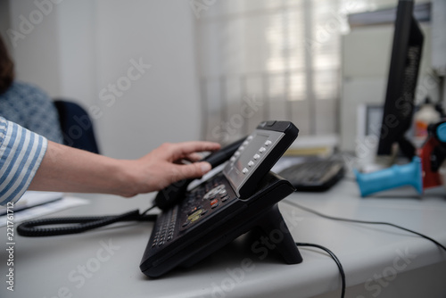 Closeup of businesswoman dialing making office phonecall, light table background. Corporate female holding telephone handle digital electronic pc connection checking daily data news, online talk job.