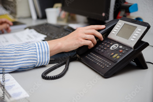 Closeup of businesswoman dialing making office phonecall, light table background. Corporate female holding telephone handle digital electronic pc connection checking daily data news, online talk job.