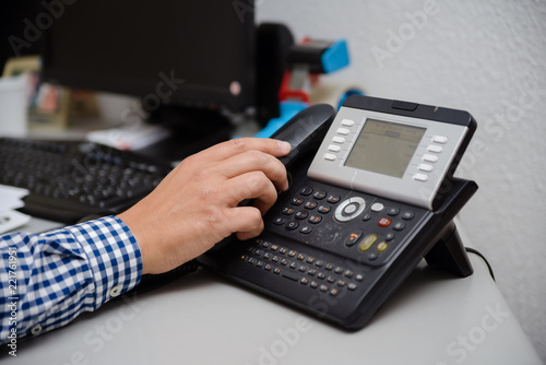 Closeup of businessman dialing making office phonecall, light table background. Corporate male holding telephone handle digital electronic pc connection checking daily data news, online chat talk job.